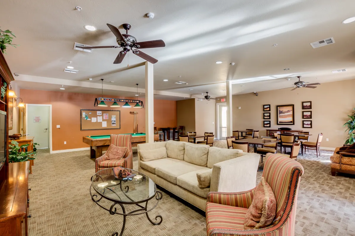 A spacious open-concept room that seamlessly integrates a sofa, a pool table, a dining area, and decorative wall art. Ceiling fans add to the comfort, while the arrangement invites guests to socialize, relax, dine, or play games in one large communal space.