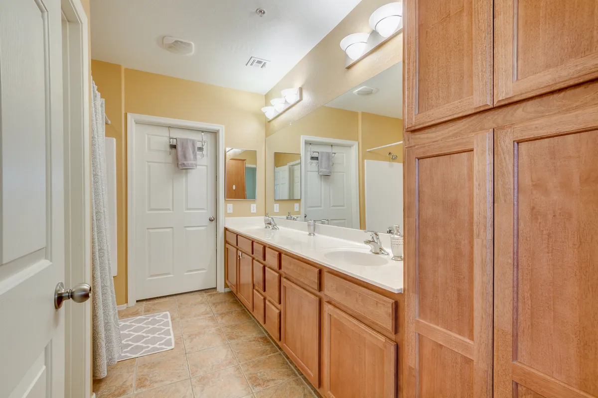 A modern bathroom with a double sink vanity, large mirrors, wood cabinetry, and elegant light fixtures. Morning sunlight enhances the inviting and functional atmosphere, ideal for daily routines or relaxation.