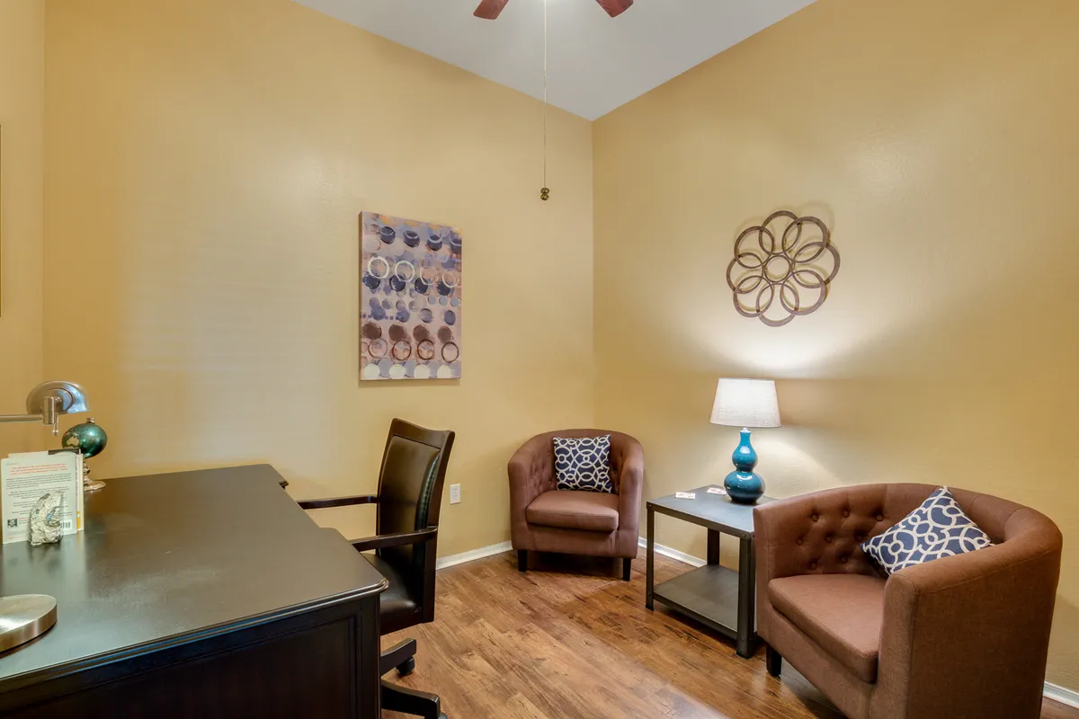 A bright and flexible room with a desk, seating area, lamp, and lively wall art. The mood is calm and productive, suitable for creative sessions, informal discussions, or quiet moments between outings.