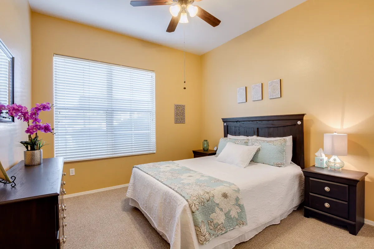 This inviting bedroom features a plush bed next to a sunlit window and a stylish nightstand with decorative items. The overall atmosphere is warm and restful, hinting at mornings spent enjoying coffee by the window or evenings spent reading and relaxing.